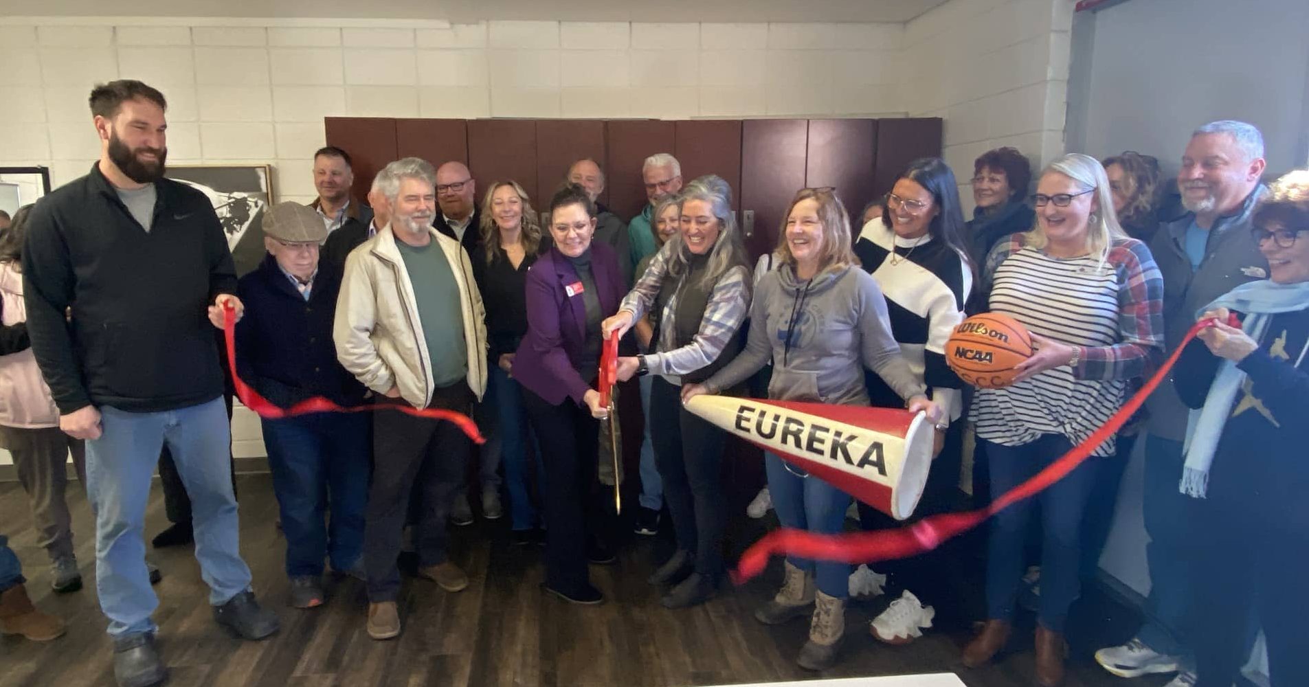 Group of adults in front of lockers cutting a red ribbon