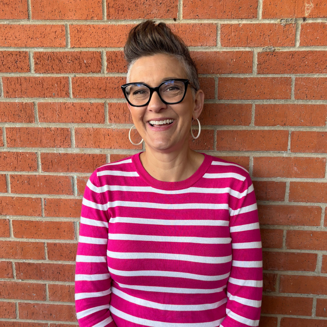 Woman in pink and white striped shirt smiling in front of brick wall